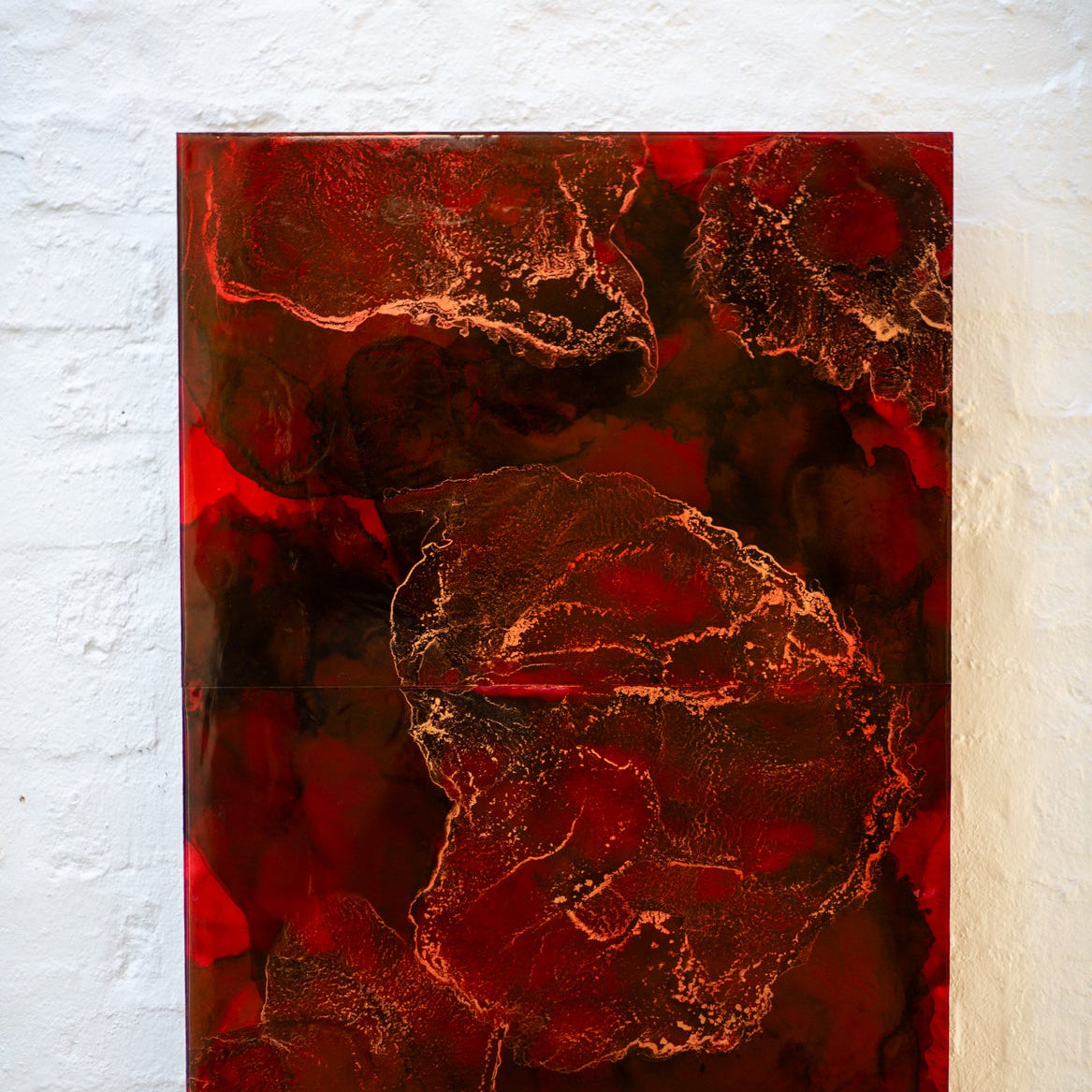 Abstract art piece with red and brown colors on a white wall